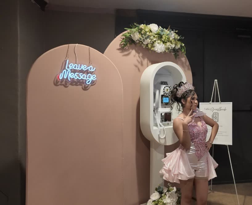 A quinceañera in a pink dress beside the booth